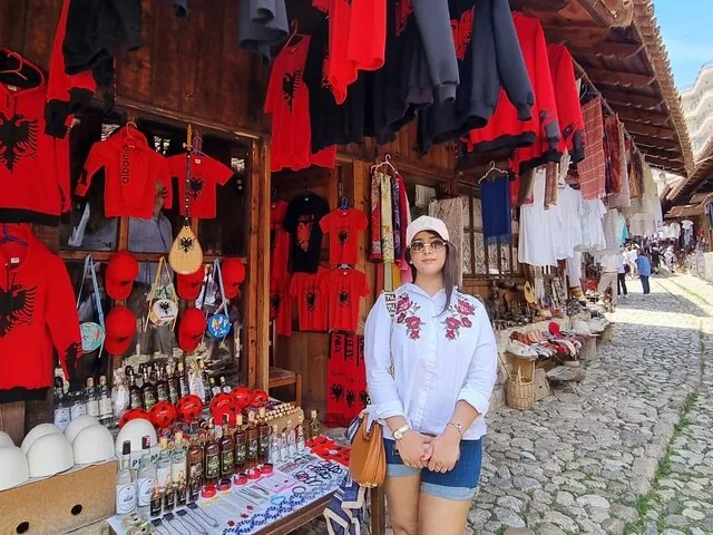 Eine Frau steht vor einem Marktstand, an dem albanische Souvenirs verkauft werden.