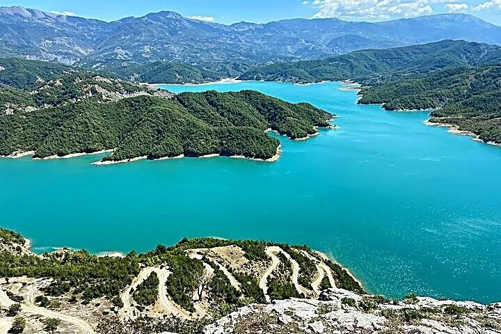 Ein weiter Blick auf das türkisfarbene Wasser des Bovilla-Sees, eingebettet in üppig grüne Berge.
