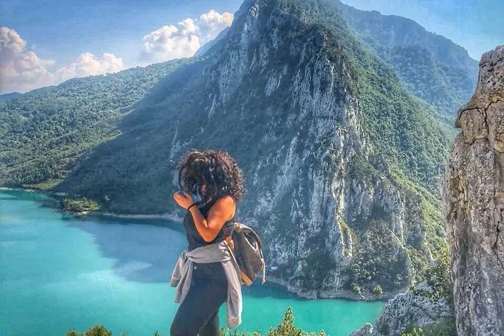 Eine Frau steht auf einem Felsvorsprung mit Blick auf den Bovilla-See und den Berg Gamti.