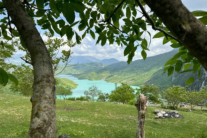 Ein Blick auf das türkisfarbene Wasser des Bovilla-Sees, eingerahmt von Bäumen im Vordergrund.