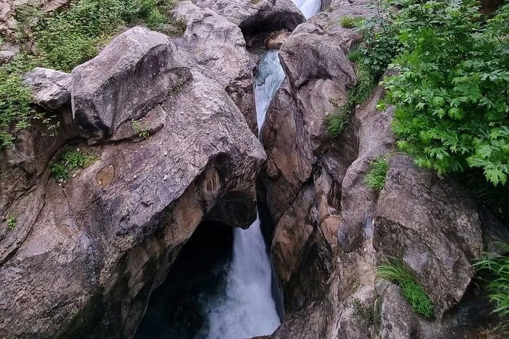 Ein schmaler Bach fließt durch eine tiefe, felsige Schlucht mit kleinen Wasserfällen.