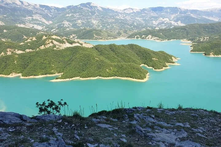Weiter Blick auf das türkisfarbene Wasser des Bovilla-Sees umgeben von grünen Bergen.